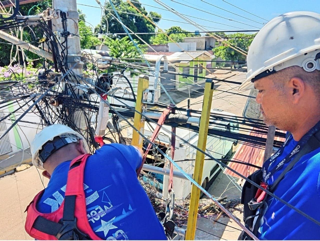 Dos técnicos de Cantv con casco trabajan en el cableado de un poste