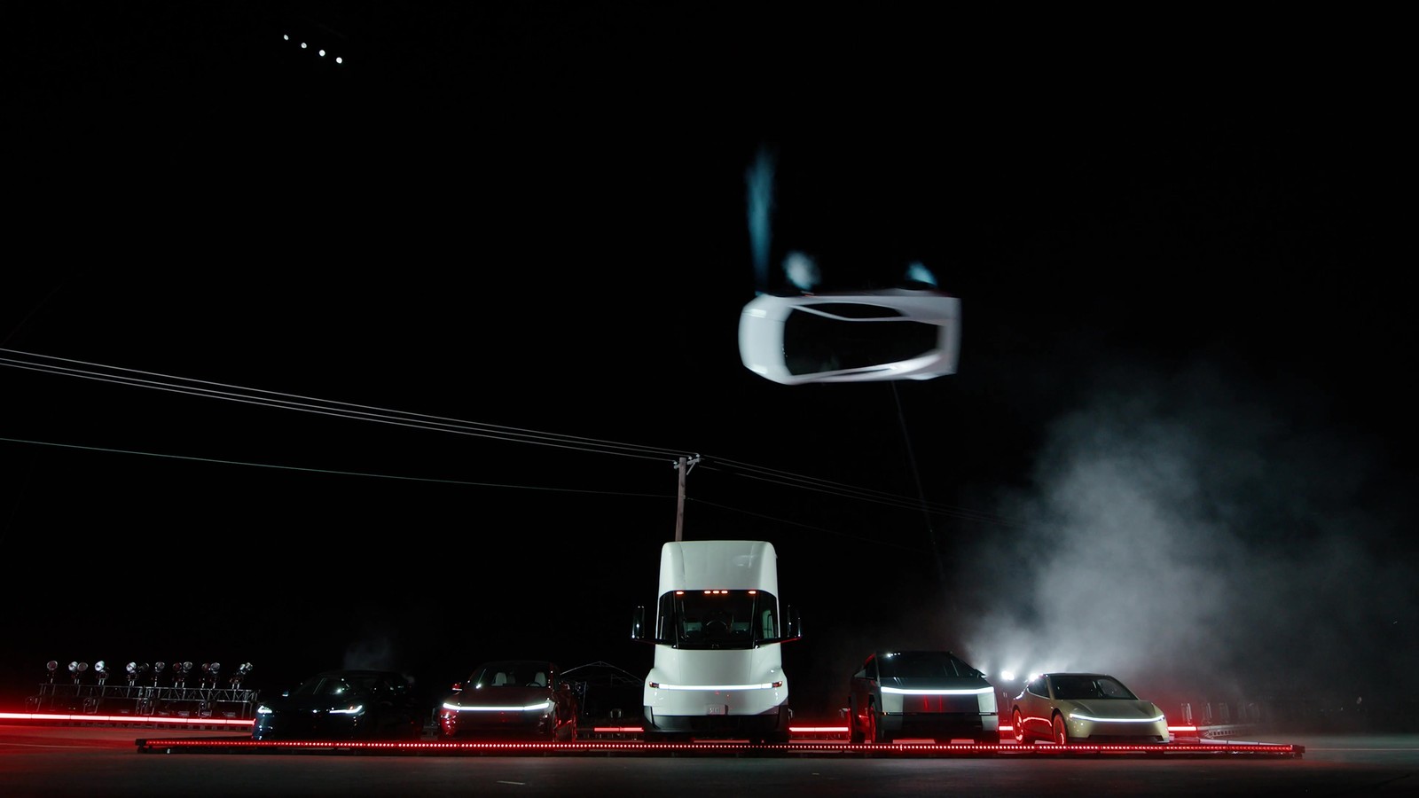 El Roadster blanco en el aire, en pleno giro, por encima de una fila de vehículos de Tesla con un camión Semi al centro